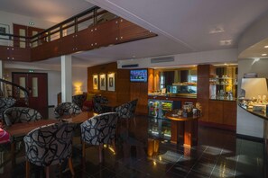 A hotel lobby with a bar area, seating with patterned chairs, a television, and a staircase. - Van der Valk Hotel Paris CDG Airport (Roissy-en-France)