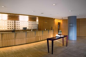 A modern reception area with a wooden reception desk, a column with Starbucks branding, and a patterned wall. - Van der Valk Hotel Paris CDG Airport (Roissy-en-France)