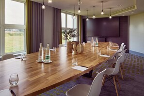 A conference room with a long wooden table, white chairs, and a large screen. - Van der Valk Hotel Paris CDG Airport (Roissy-en-France)
