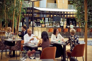 An outdoor dining area with tables and chairs, surrounded by greenery and a bar area in the background. - Van der Valk Hotel Paris CDG Airport (Roissy-en-France)