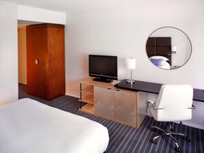 Une chambre d’hôtel comprenant un lit, un bureau avec une télévision, une chaise, un miroir et une armoire.