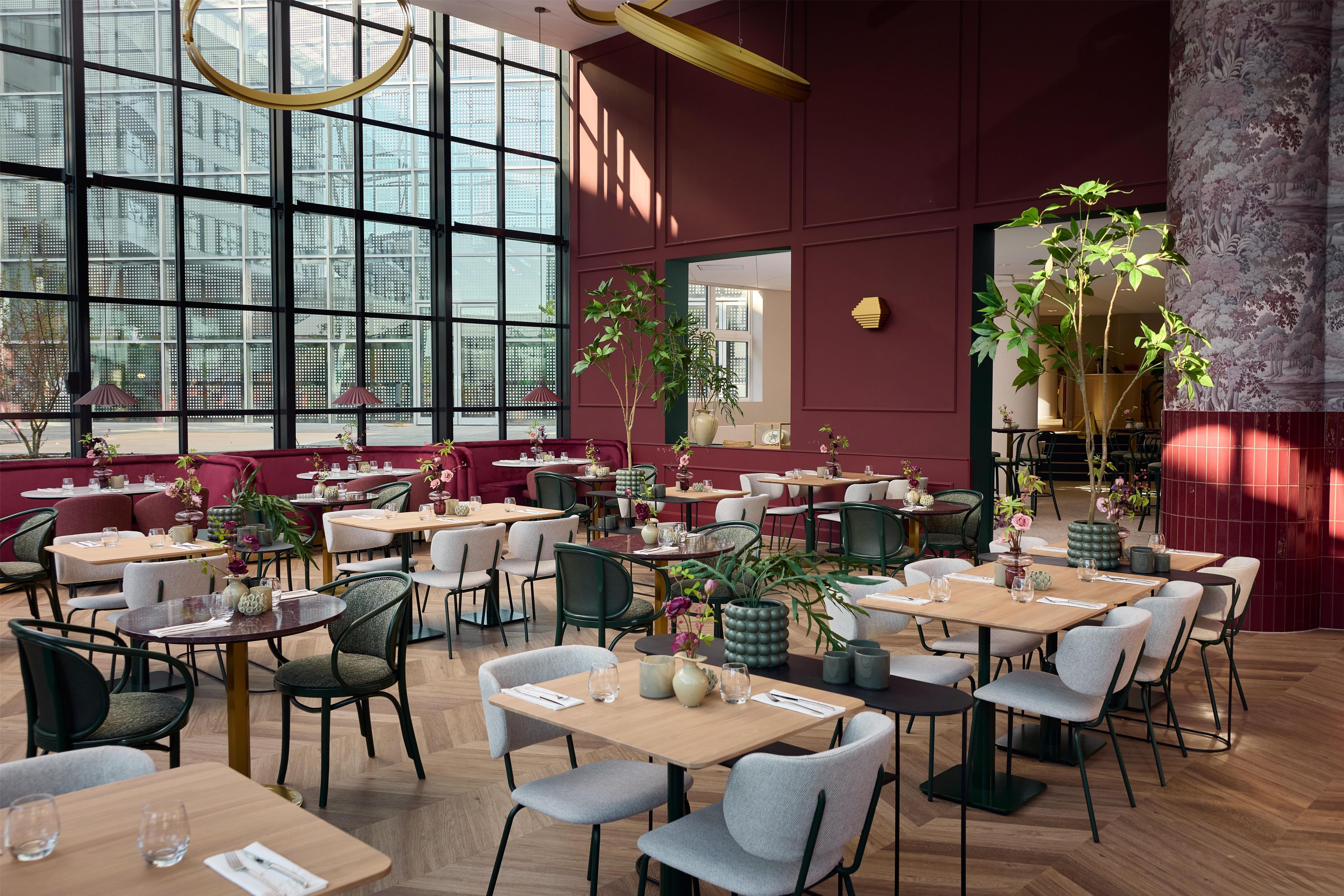 Un ristorante con diversi tavoli e sedie, ampie finestre e piante da interno.