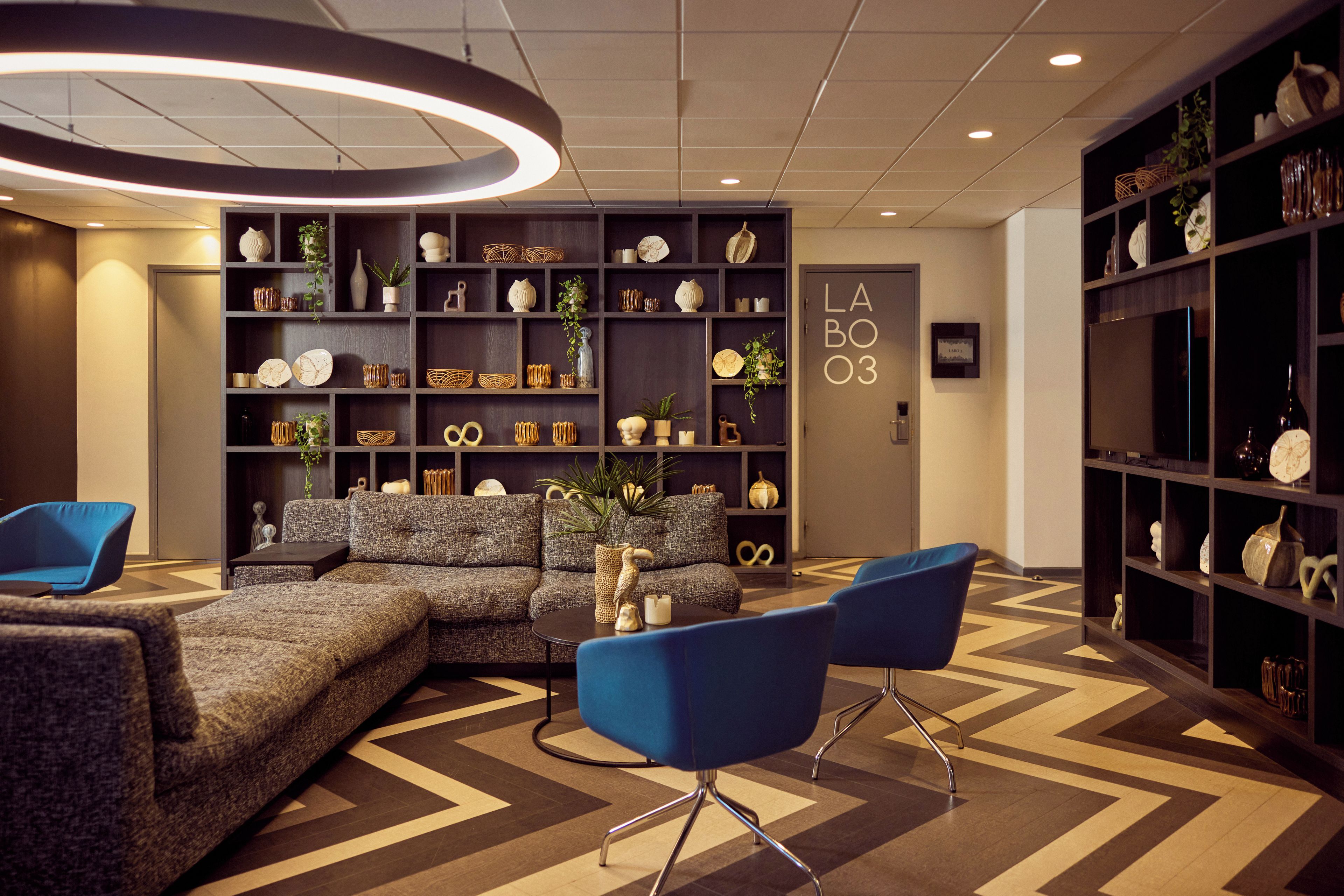 A modern lobby with a sectional sofa, blue chairs, and a decorative bookshelf.