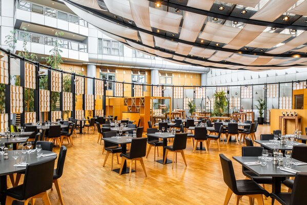 A spacious indoor dining area with multiple tables and chairs, large windows, and a high ceiling with a unique fabric design. - Van der Valk Hotel Paris CDG Airport (Roissy-en-France)