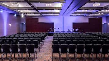 Een congreszaal met rijen stoelen, een podium en kroonluchters.