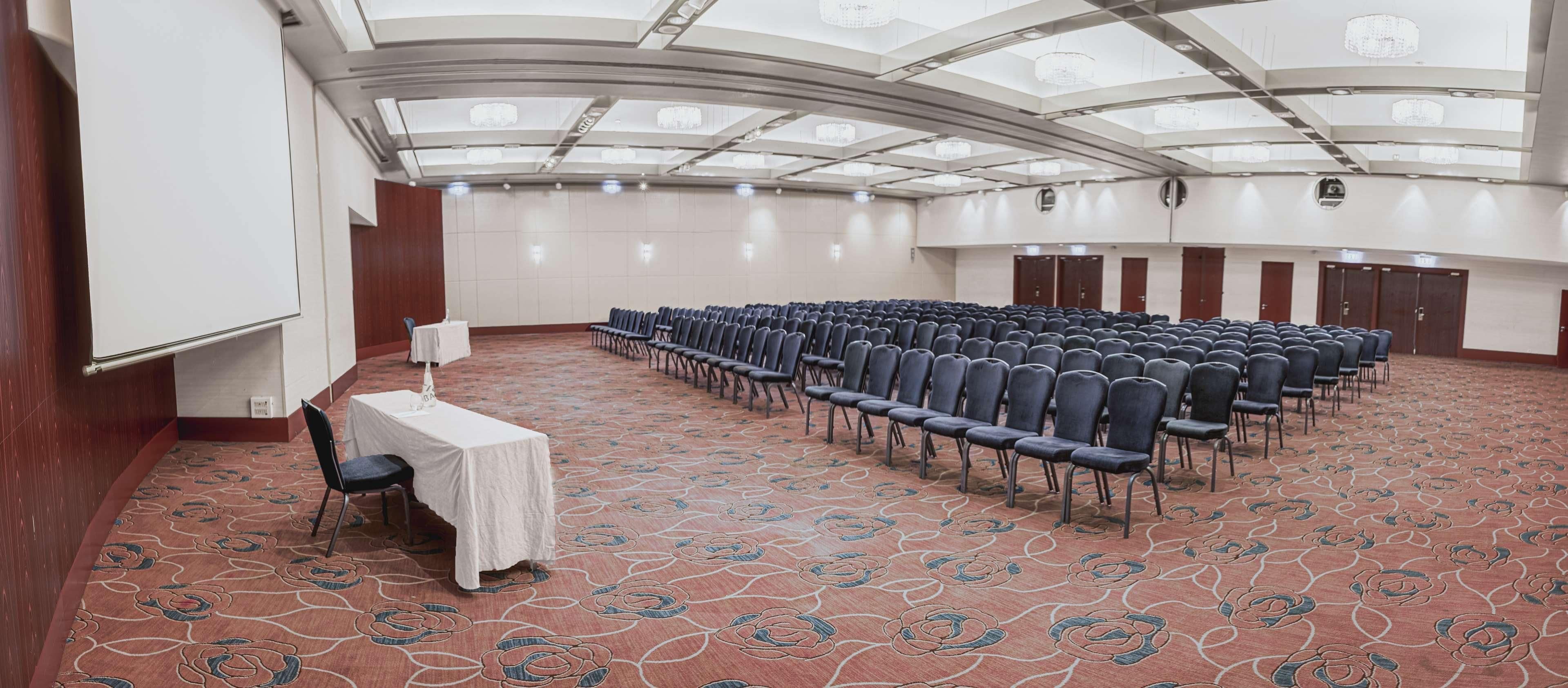 A conference room with rows of chairs, a white table with a cloth, and a patterned carpet.