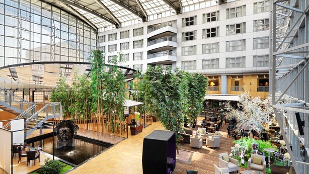 A spacious atrium with a central water feature, multiple seating areas, and a variety of indoor plants. - Van der Valk Hotel Paris CDG Airport (Roissy-en-France)