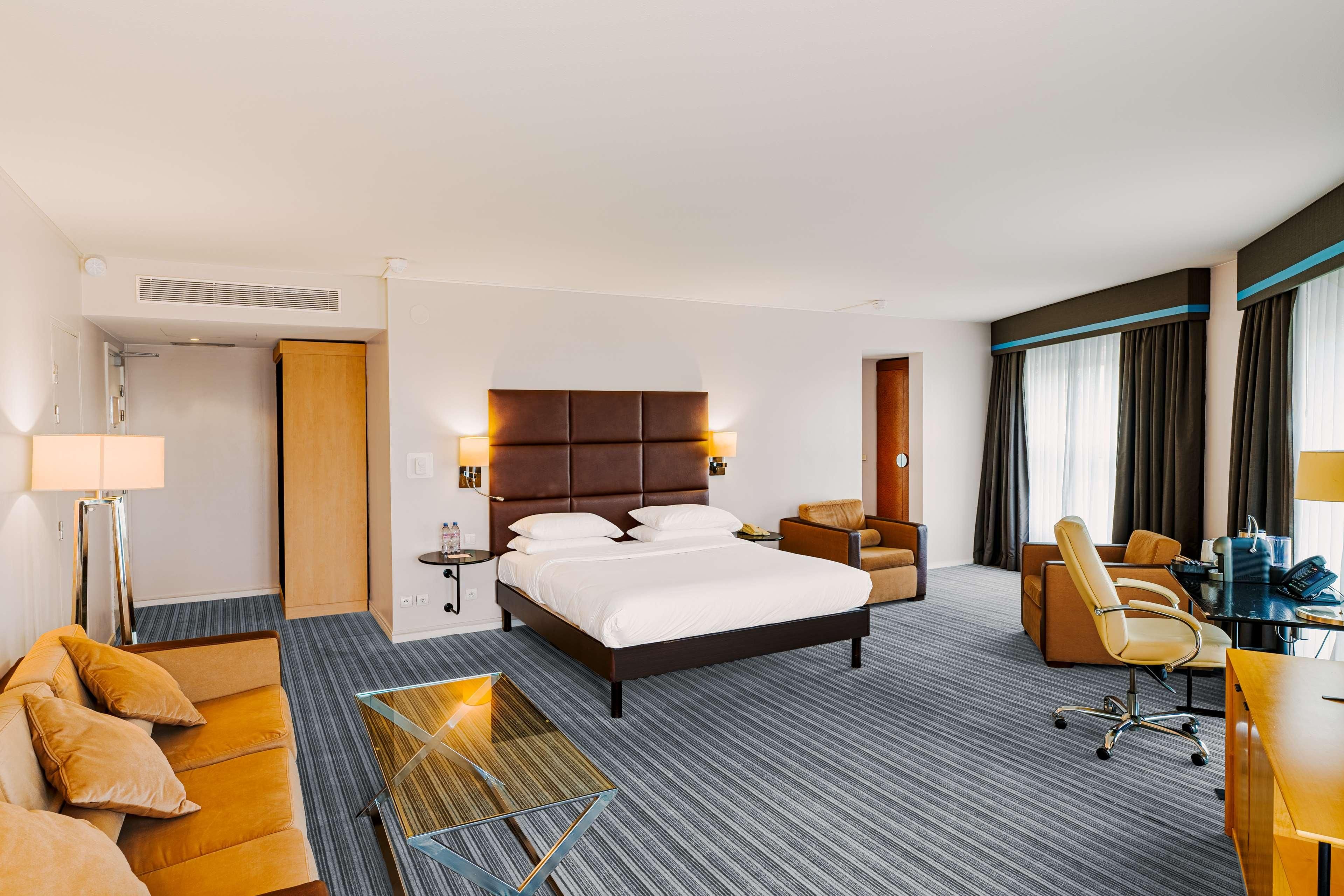 A hotel room with a large bed, a desk, a chair, a sofa, and a small table.