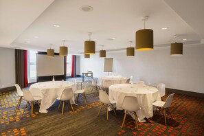 A conference room with round tables, white chairs, and brown pendant lights.