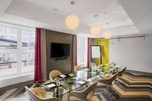 Una sala conferenze moderna con tavolo in vetro, sedie confortevoli, una TV a schermo piatto e ampie finestre con vista sull'esterno.