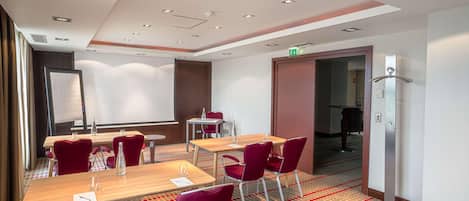 Un salón de conferencias con mesas, sillas y una pantalla para proyector.