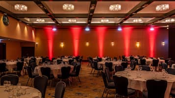 Een feestzaal met ronde tafels, zwarte stoelen, kroonluchters en rood sfeerverlichting.