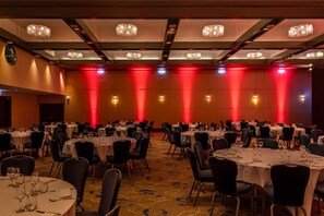 Une salle de banquet avec des tables rondes, des chaises noires, des lustres et un éclairage d’ambiance rouge.
