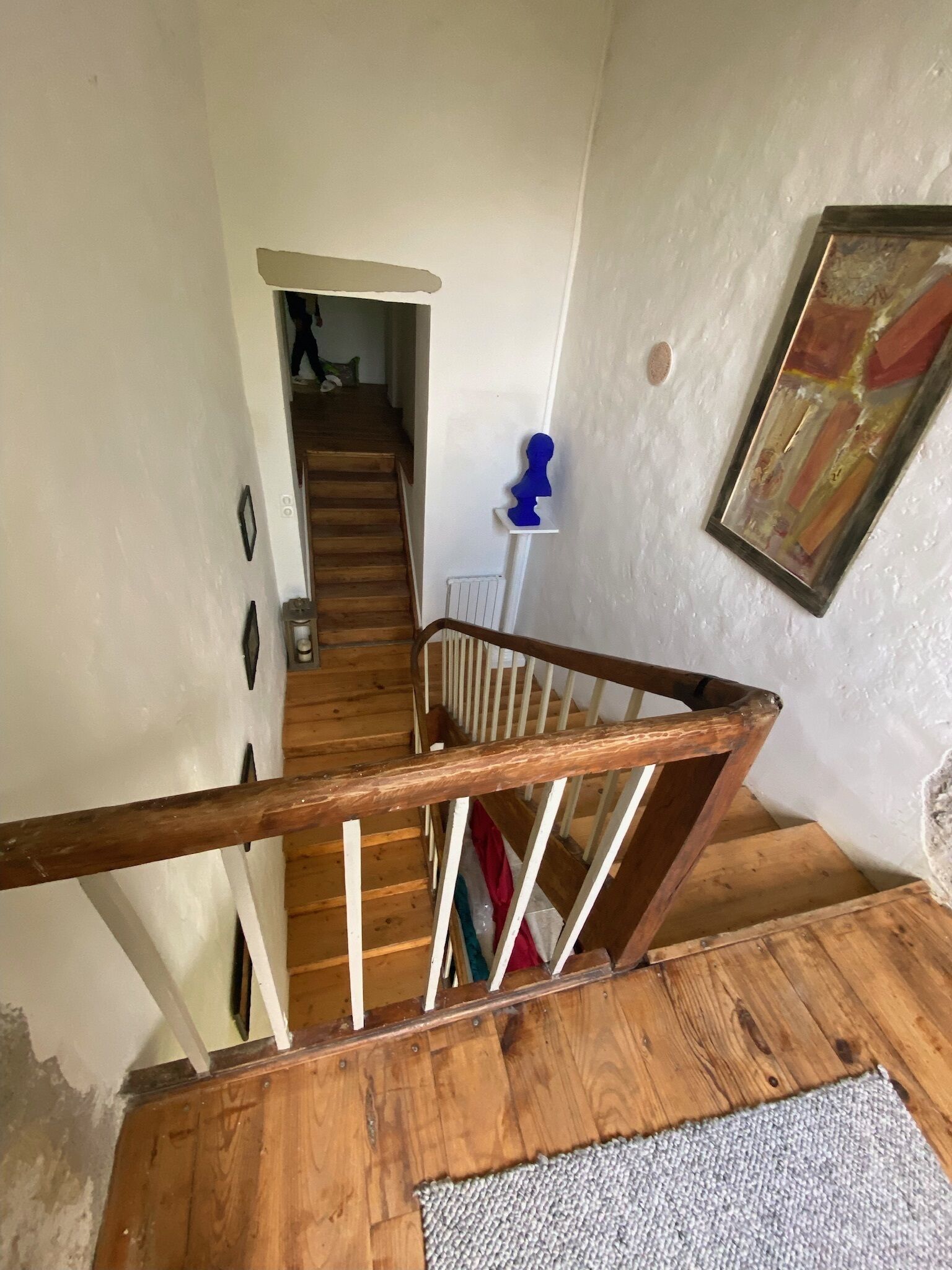 A wooden staircase with a white railing leading to a landing. A blue decorative item is on a white shelf on the landing.