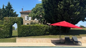 Ein Swimmingpool mit einem roten Sonnenschirm, Liegestühlen und einem Steinhaus im Hintergrund.