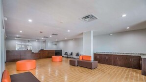 A spacious lobby with a wooden floor, orange and brown seating, a reception desk, and a large window. - OYO Hotel Orlando Airport (Orlando)