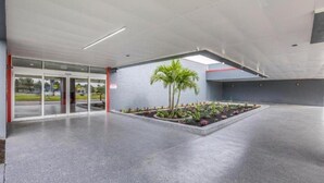 A modern building entrance with glass doors, a concrete floor, and a small garden area with palm trees and plants. - OYO Hotel Orlando Airport (Orlando)