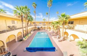Relax by the central pool surrounded by palm trees and lounge chairs, with arched walkways and balconies nearby.