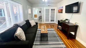 A living room with a black sofa, a wooden coffee table, a striped rug, and a dark wooden side table with a plant. - Historic Avenues Downtown Loft (Salt Lake City)