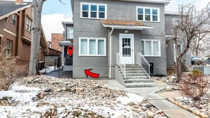A two-story house with a front porch, a red arrow pointing to the entrance, and a snow-covered ground. - Historic Avenues Downtown Loft (Salt Lake City)