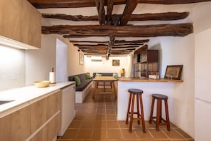 A kitchen with a wooden ceiling, a dining area with a table and chairs, and a bar area with stools.