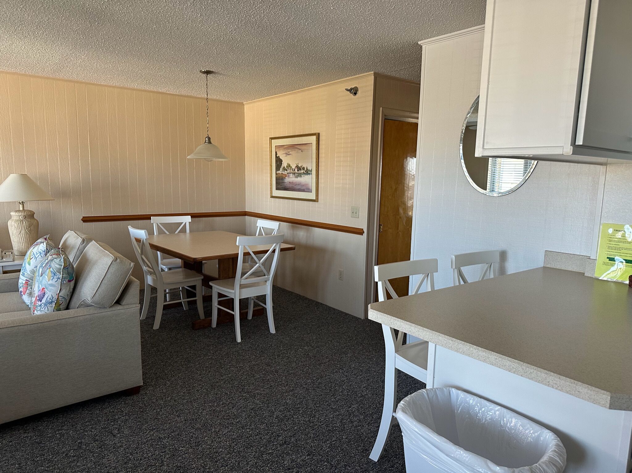 A compact kitchen with a dining table, chairs, a small sofa, and a trash bin.