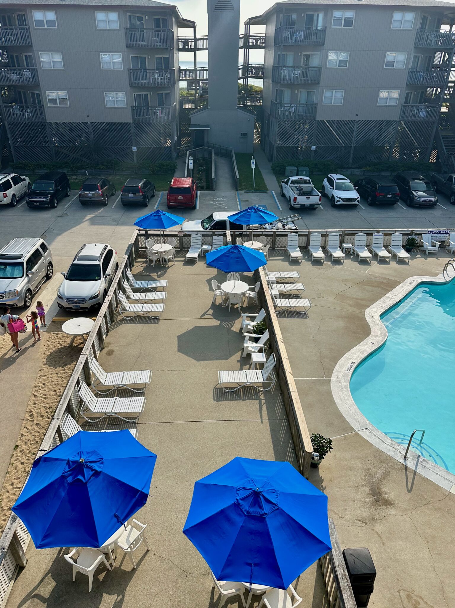 A rooftop pool area with lounge chairs and umbrellas, surrounded by a parking lot with various vehicles.