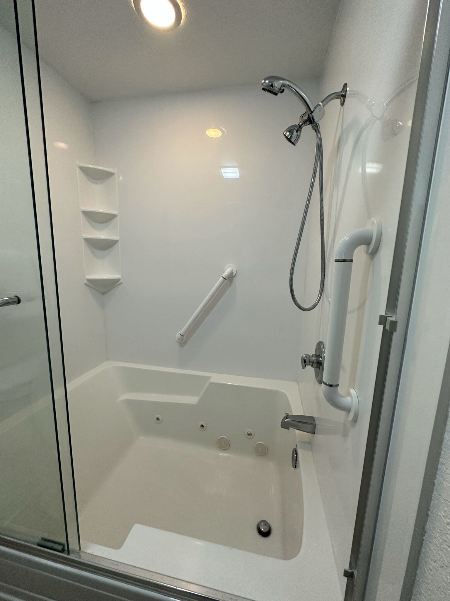A modern bathroom with a glass shower enclosure, a white bathtub, and a built-in shelf unit.