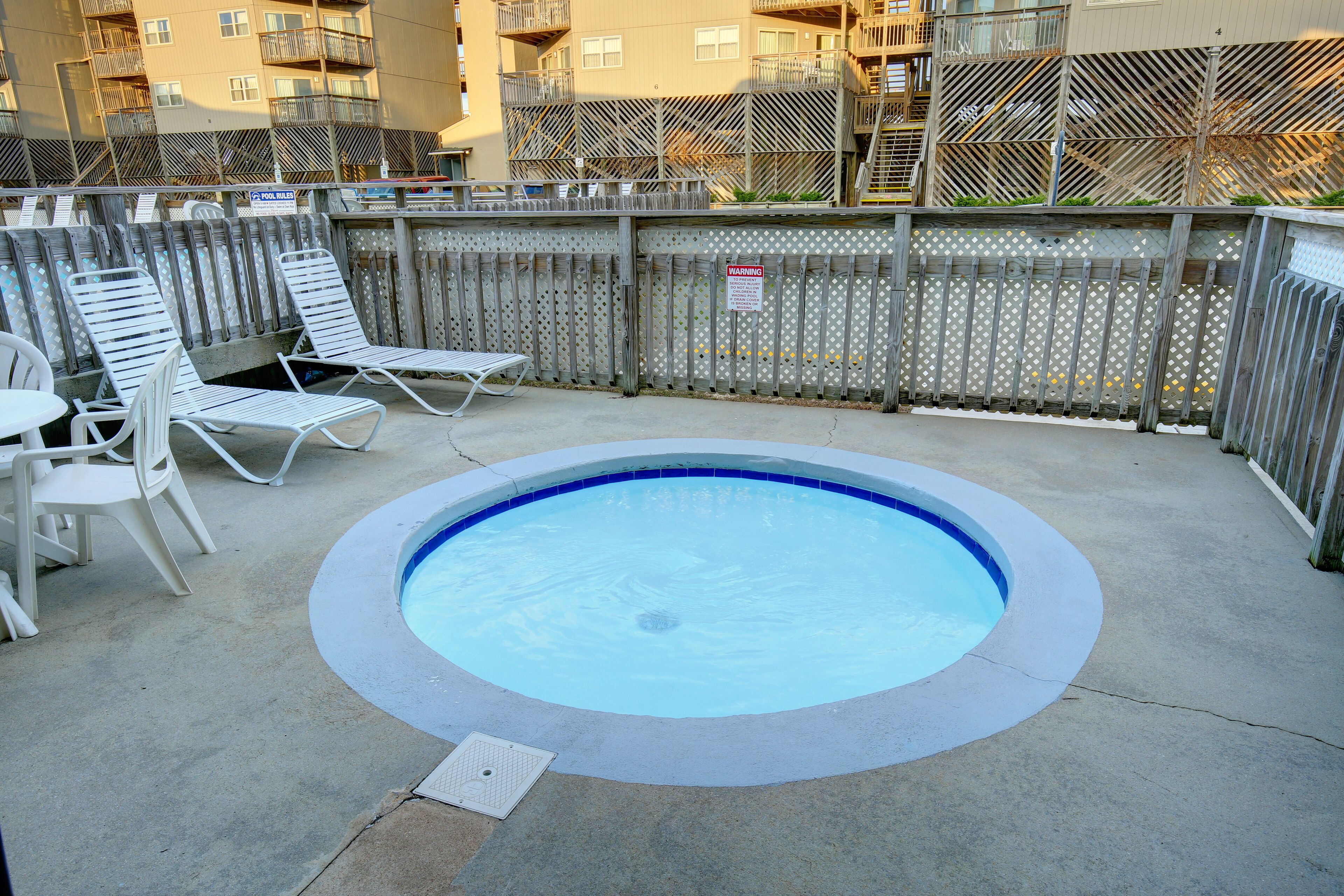Une petite piscine extérieure avec des chaises longues et une clôture en métal.