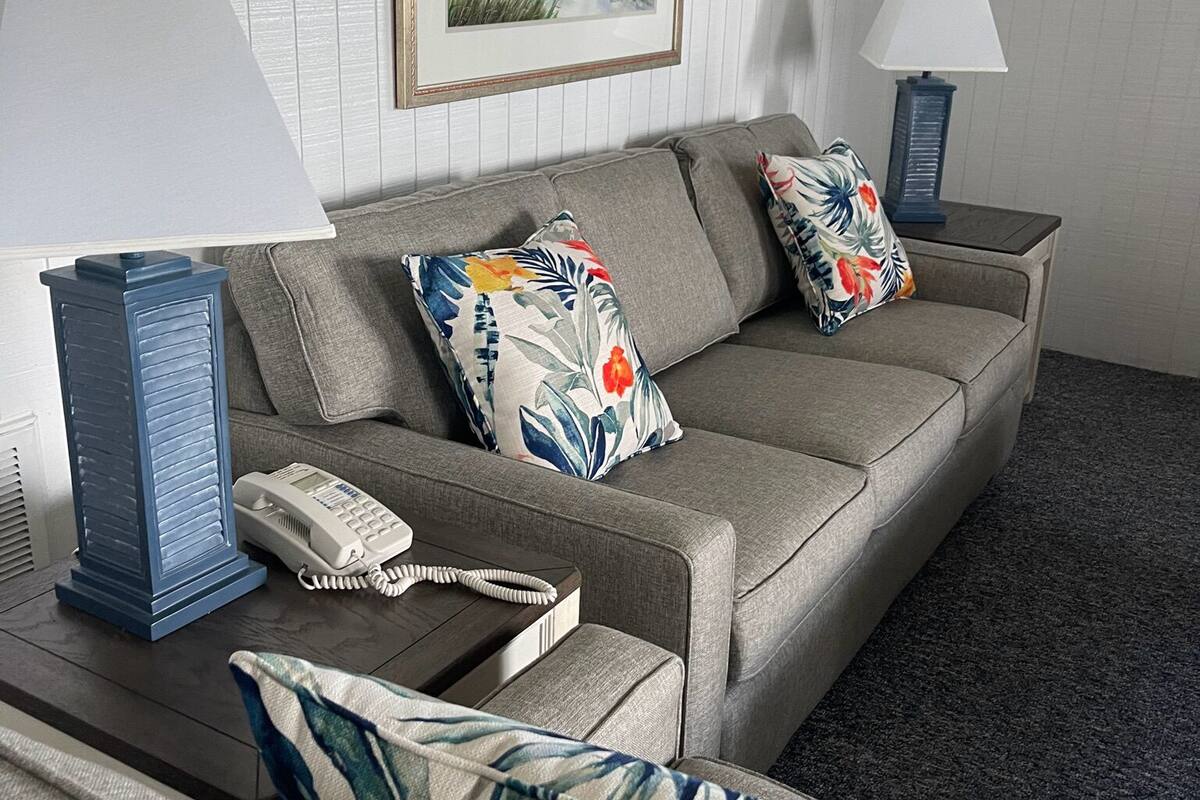 A modern living room with a grey sofa, floral cushions, a framed beach painting, a blue lamp, and a telephone on a wooden side table.