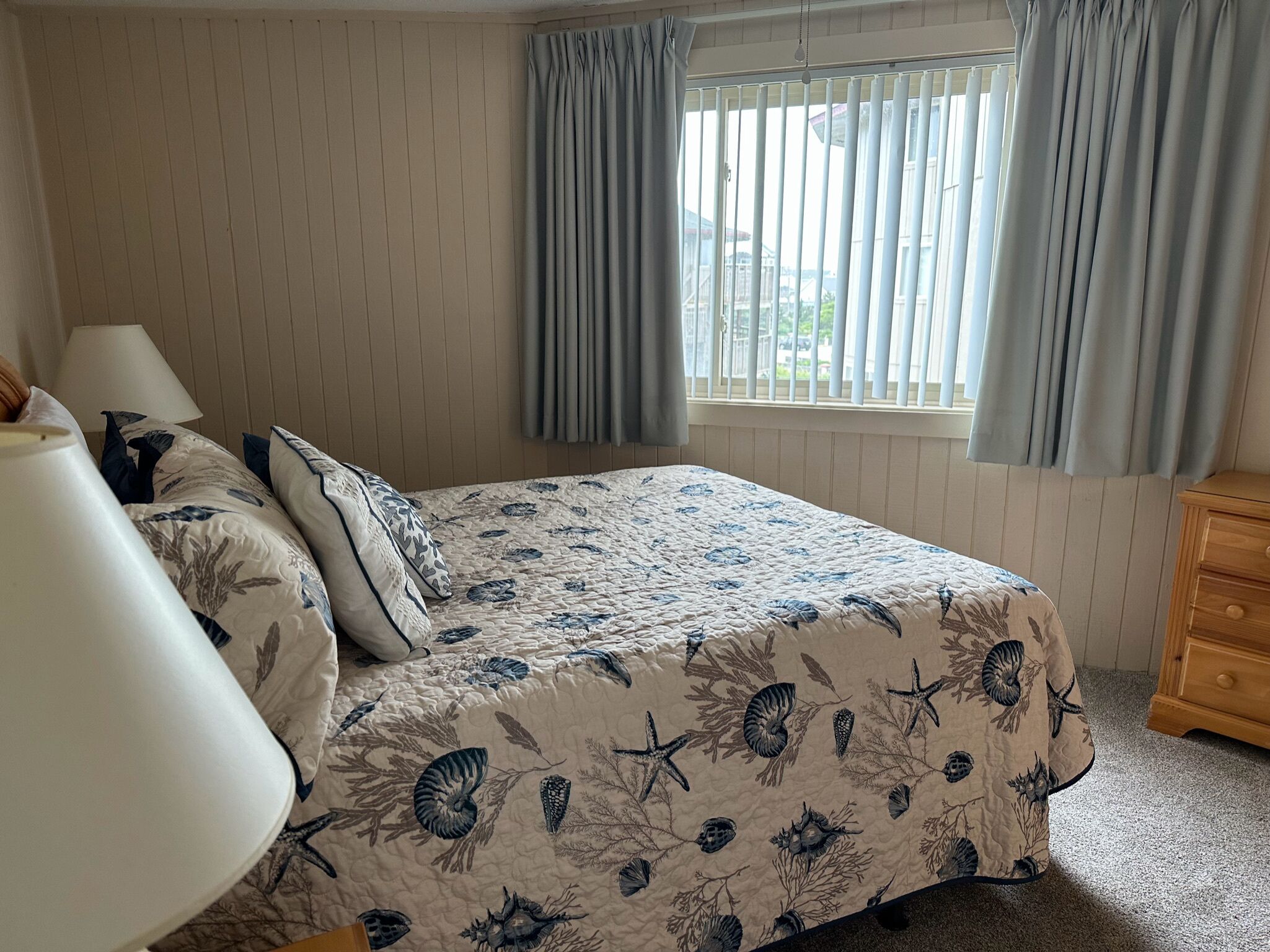 Une chambre à coucher avec un lit, une table de chevet, une lampe et une fenêtre avec des rideaux.