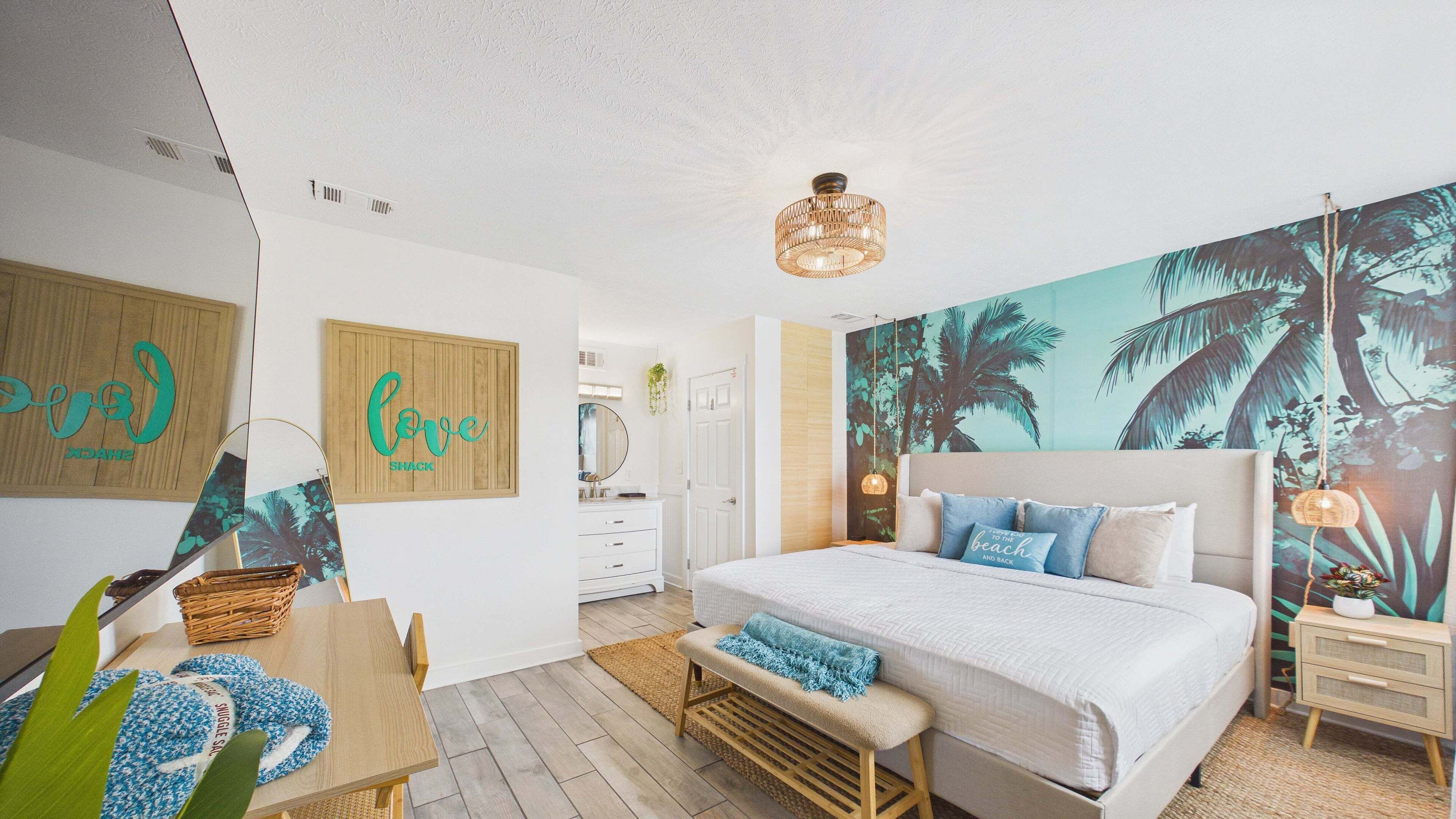 A bedroom with a large bed, a wall mural, a wooden bench, and a small table with a basket.