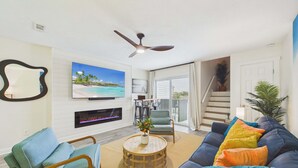 A living room with a TV, fireplace, ceiling fan, and a staircase leading to a balcony.