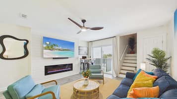 A living room with a TV, fireplace, ceiling fan, and a staircase leading to a balcony.