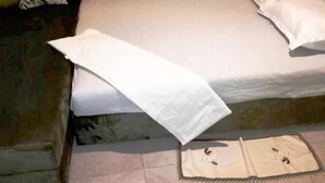 Un lit recouvert d’un drap blanc et d’une couverture blanche, un oreiller et une table de chevet sur laquelle repose un petit objet décoratif.