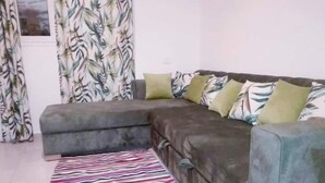 Un salon avec un canapé d’angle, un tapis à rayures et des rideaux à motifs.