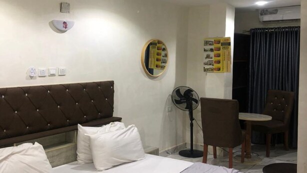 Ein Hotelzimmer mit einem Bett, einem Sessel, einem Tisch, einem Ventilator und einer Wand mit einem Korkbrett.