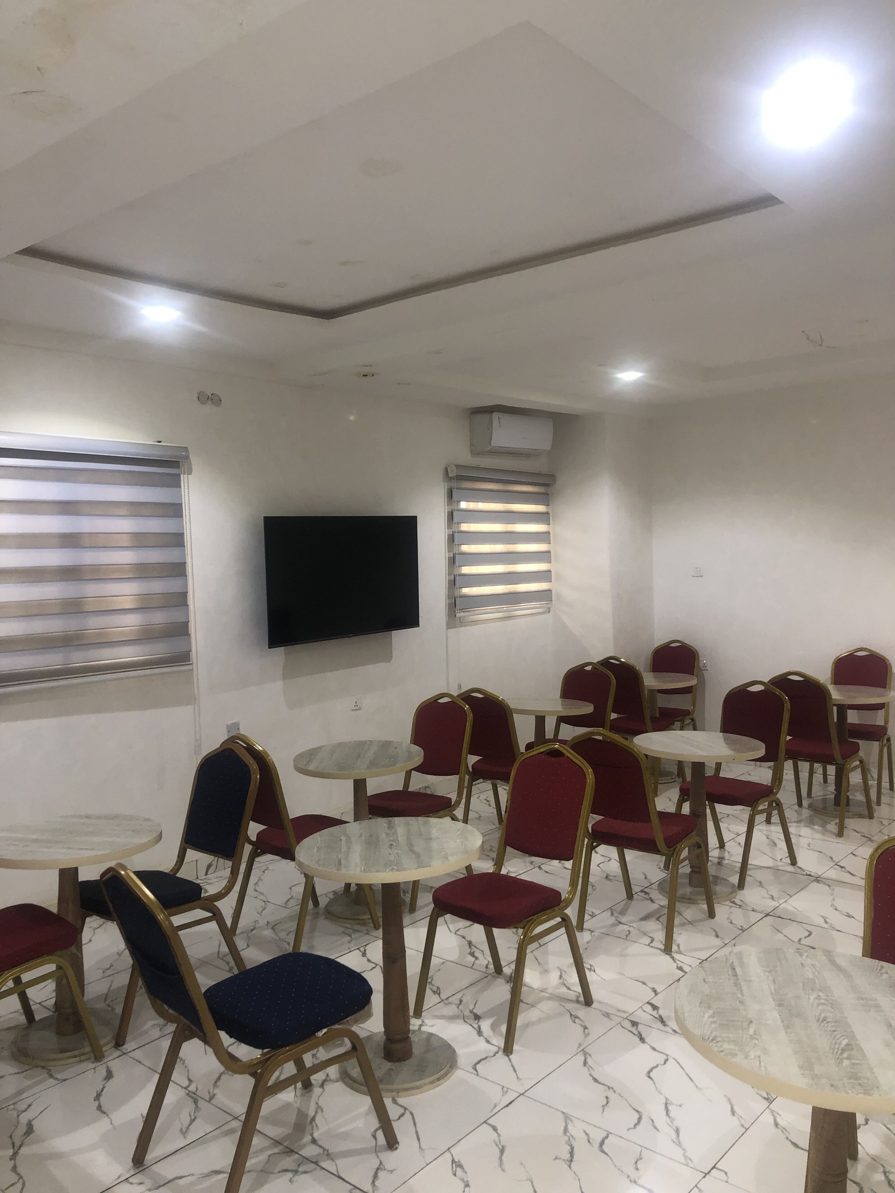 A room with multiple round tables and chairs, a flat-screen TV mounted on the wall, and air conditioning units on the ceiling.