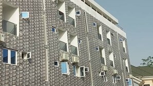 Ein mehrstöckiges Gebäude mit einer strukturierten Fassade, mehreren Balkonen und Klimaanlagen.
