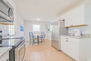 A modern kitchen with white cabinets, a stainless steel refrigerator, and a dining area with blue chairs.