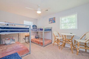 A bunk bed room with a ceiling fan, two windows with blinds, a small table, and two wicker chairs.