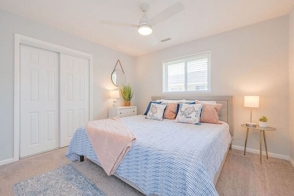A bedroom with a bed, bedside tables, a ceiling fan, a window, and a door.