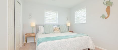 A bedroom with a bed, two nightstands, a ceiling fan, and two windows.