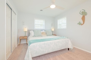 A bedroom with a bed, two nightstands, a ceiling fan, and two windows.