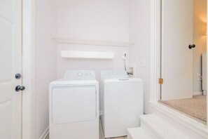 A laundry room with two white front-loading washing machines, a white shelf above them, and a white door on the left. - #Buckroe Bungalow ~Escape to the Beach 2mins Away! (Hampton)