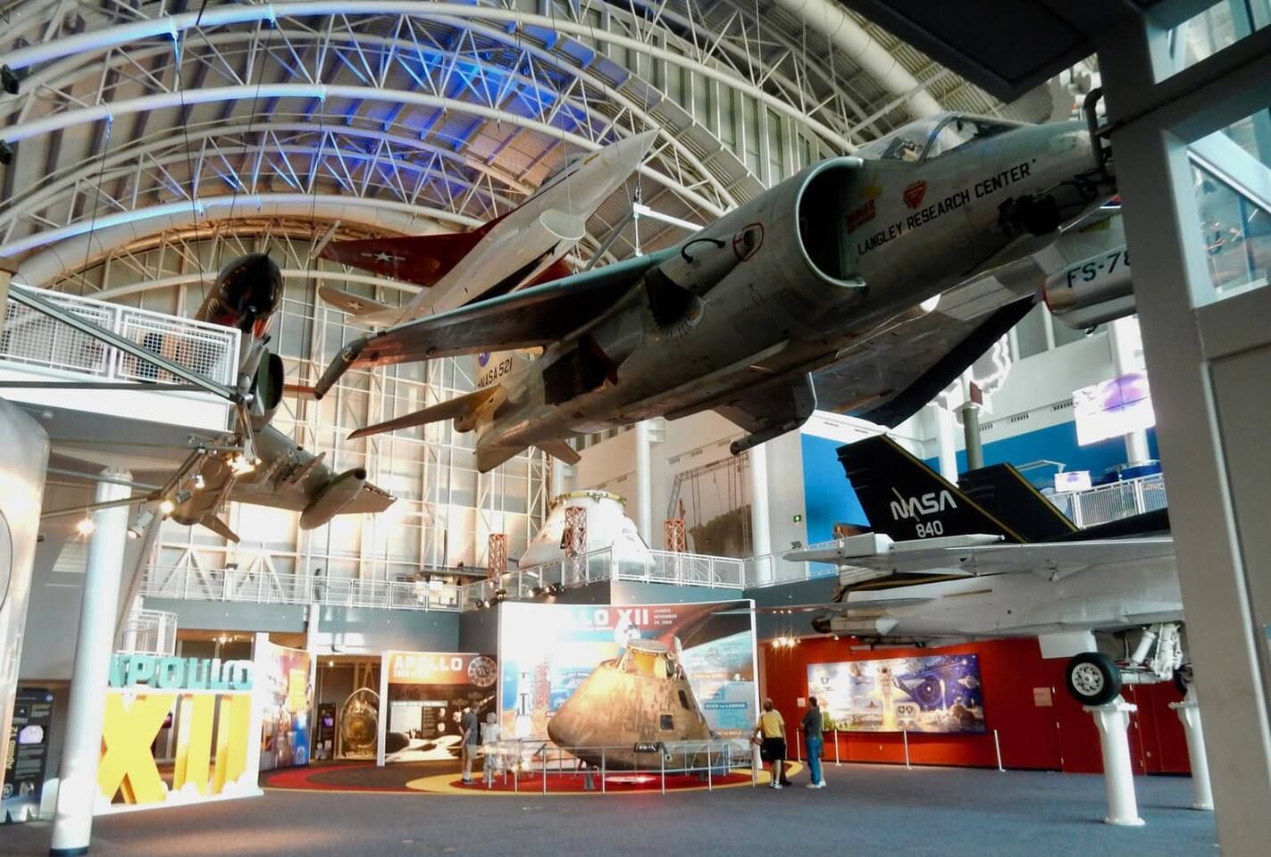 A museum interior with a large space shuttle on display, NASA branding, and a prominent Apollo exhibit.
