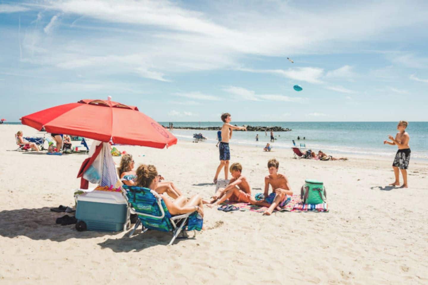 A beach scene with people relaxing under umbrellas, a cooler, and beach chairs.