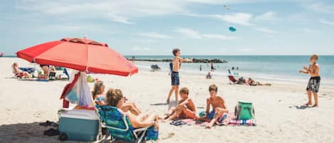 A beach scene with people relaxing under umbrellas, a cooler, and beach chairs.