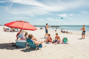 A beach scene with people relaxing under umbrellas, a cooler, and beach chairs.