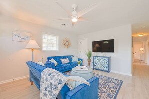 A living room with a blue sofa, a coffee table, a TV, and a ceiling fan. - #Buckroe Bungalow ~Escape to the Beach 2mins Away! (Hampton)
